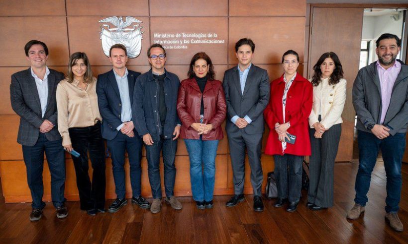 Nine people in business attire stand in a row before a wood-paneled wall with Colombia's coat of arms and the MinTIC name.