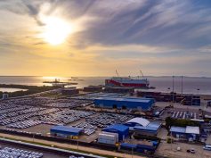 Aerial view at sunset of a roll-on/roll-off vehicle carrier docked at Puerto Bahía with rows of cars staged for loading.