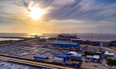 Aerial view at sunset of a roll-on/roll-off vehicle carrier docked at Puerto Bahía with rows of cars staged for loading.
