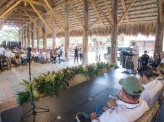 A speaker at a podium addresses an audience under a thatched open-air pavilion in Quimbaya, Quindío