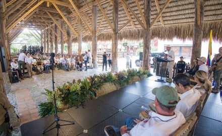 A speaker at a podium addresses an audience under a thatched open-air pavilion in Quimbaya, Quindío