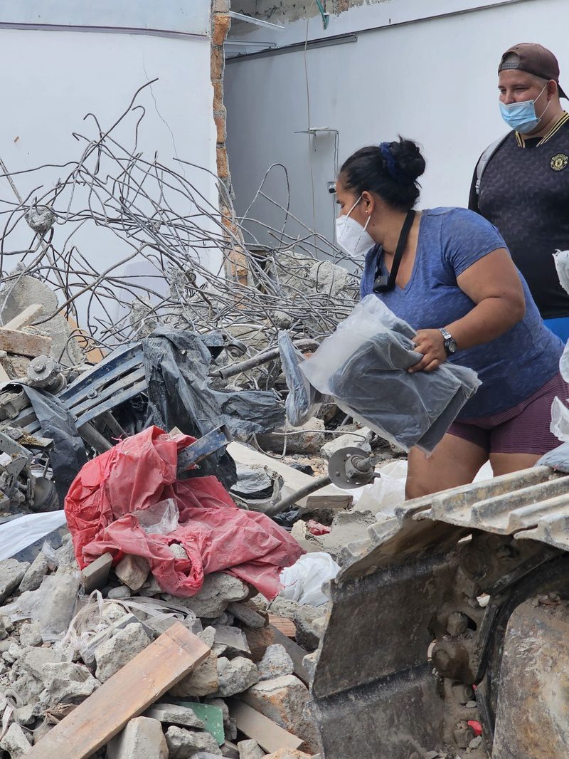 A woman holds a salvaged item while searching rubble as another volunteer looks on.