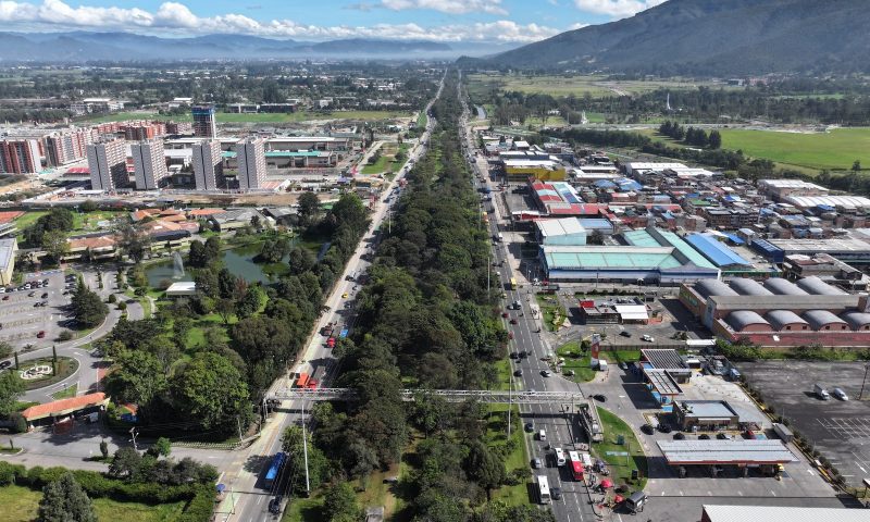 Aerial view of a tree-lined divided highway with TransMilenio buses and a pedestrian bridge in northern Bogotá