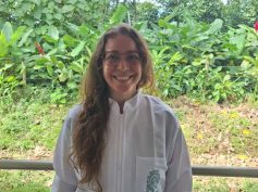 A researcher in a white Universidad de Antioquia lab coat stands in front of dense tropical vegetation.