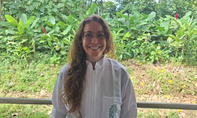 A researcher in a white Universidad de Antioquia lab coat stands in front of dense tropical vegetation.