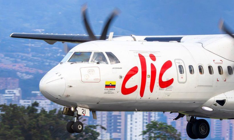 Clic ATR 42-600 in flight with landing gear down near Olaya Herrera Airport, Medellín high-rises behind