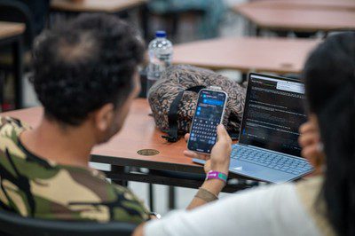 An attendee holds a smartphone beside an open laptop showing lines of text