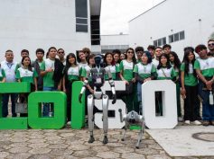 Students and adults stand behind large green and white COL5.0 letters with a humanoid robot and a robot dog in front