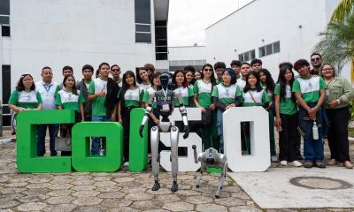 Students and adults stand behind large green and white COL5.0 letters with a humanoid robot and a robot dog in front