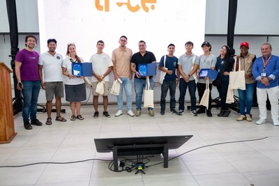 A group of people stands in a row in front of a screen, several holding blue cases and tote bags