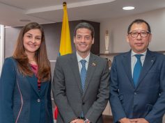 Commerce Minister Mauricio Gómez Amín stands between a woman and a man wearing a Mazda lapel pin in an office.