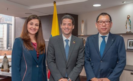 Commerce Minister Mauricio Gómez Amín stands between a woman and a man wearing a Mazda lapel pin in an office.