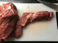 Two raw cuts of beef on a white cutting board next to a kitchen knife