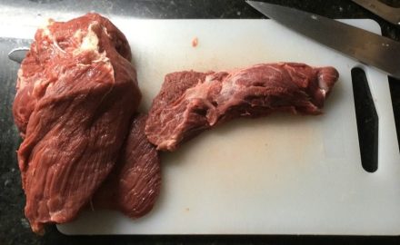 Two raw cuts of beef on a white cutting board next to a kitchen knife