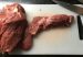 Two raw cuts of beef on a white cutting board next to a kitchen knife