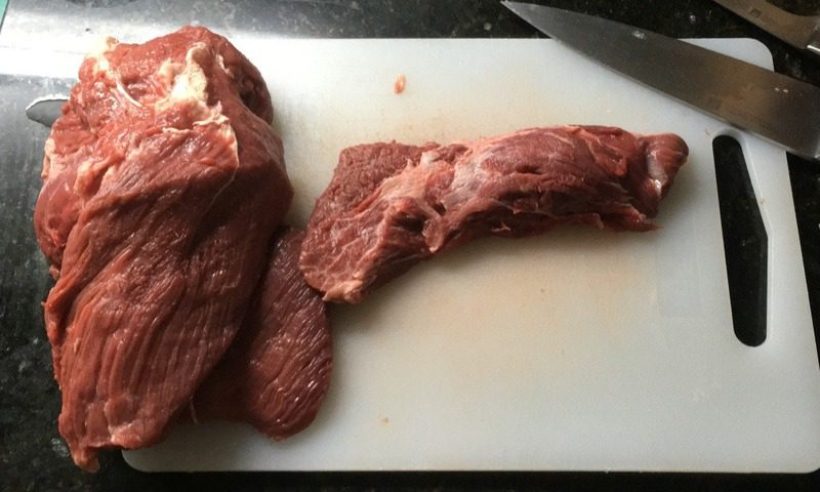 Two raw cuts of beef on a white cutting board next to a kitchen knife
