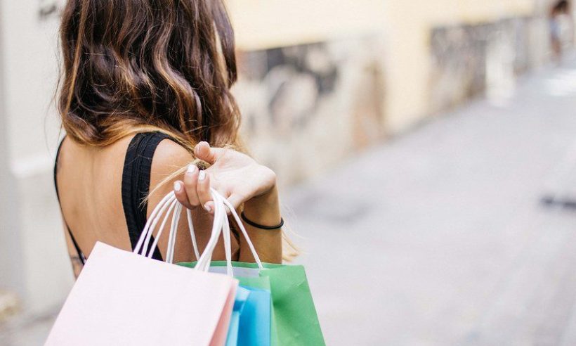 A shopper carries colorful shopping bags along a city street.