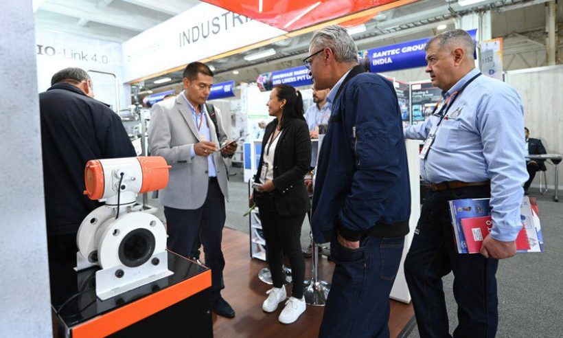Visitors and exhibitors talk at an industrial automation stand, with banners for Indian exhibitors in the background