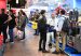 Visitors walk through a trade fair aisle lined with metalworking machinery, including industrial band saws