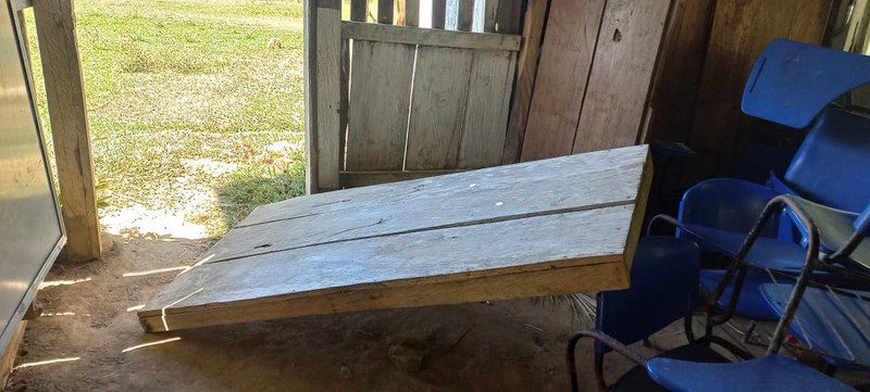 Detached wooden panel lying on the dirt floor beside blue desk-chairs