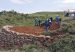 Workers in hard hats dig at a hillside site edged with a sandbag wall.