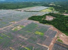 Aerial view of rows of solar panels at the Puerta de Oro solar park, with forest and hills in the background