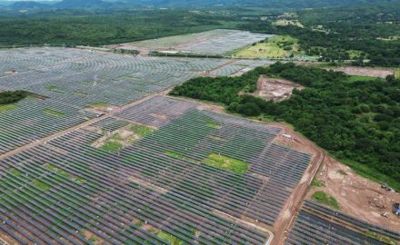 Aerial view of rows of solar panels at the Puerta de Oro solar park, with forest and hills in the background